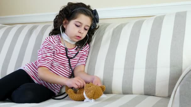 Little girl with sore throat examining her ill bear toy with a stethoscope - Кадры, видео