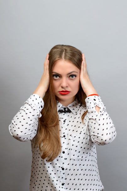 Portrait of a young woman covering her ears over gray background. Looking at camera - Photo, image