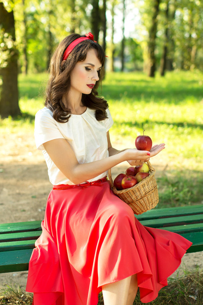 glückliches Mädchen, das auf einer Bank sitzt und einen Korb mit Äpfeln hält - Foto, Bild