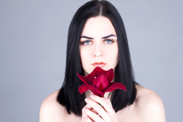Face of a woman with black hair and red flower. Beauty treatment concept. - Zdjęcie, obraz