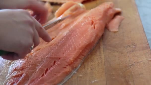 Chef cuts up the pink salmon fish by knife on the wooden board on the table - Footage, Video