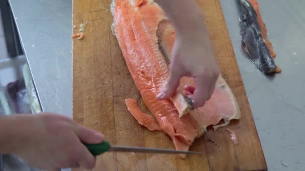 Cook cuts up the fish on the wooden board by knife in the kitchen - Footage, Video