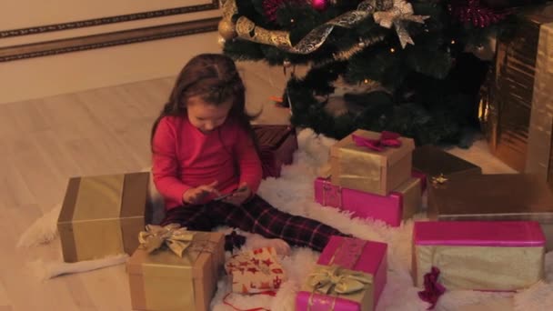 Girl Playing in Smartphone by Christmas Tree - Materiał filmowy, wideo