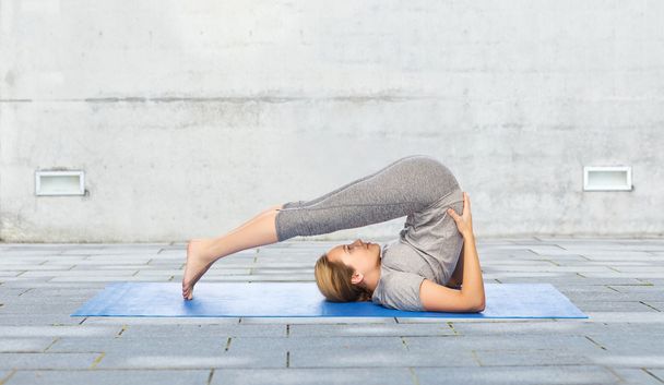 woman making yoga in plow pose on mat outdoors - Foto, Imagen