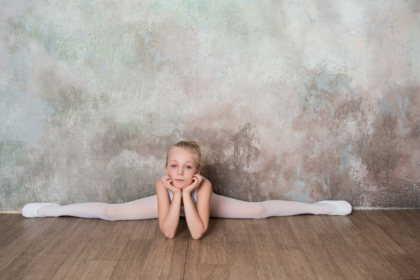 Little ballet dancer sitting on the splits in white bathing suit - Фото, изображение