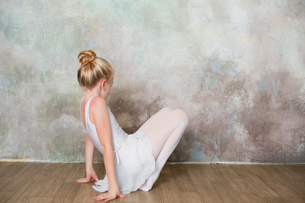 Little ballet dancer doing stretching before class in a white bathing suit - Foto, Bild
