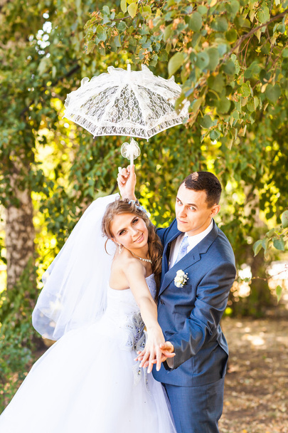 Μόλις παντρεμένο ζευγάρι κρατώντας λευκή ομπρέλα - Φωτογραφία, εικόνα