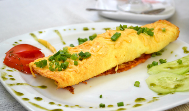 Вкусный омлет с сыром и зеленым луком подается с помидорами на белой тарелке
 - Фото, изображение