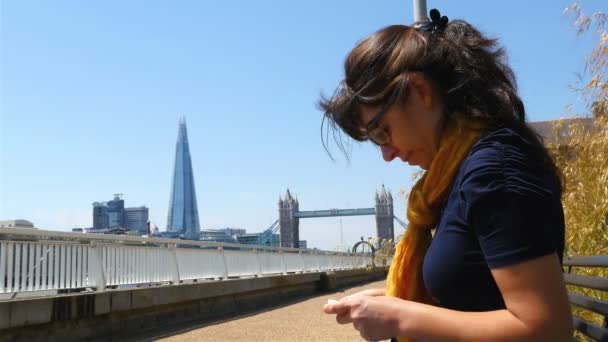 Fiatal nő küld egy sms-t egy mobiltelefonnal London Tower híddal és Shard-dal a háttérben, közelről - Felvétel, videó