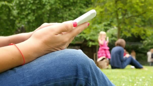 Close-up van de vrouw met behulp van mobiele telefoon zittend in een park, handen alleen - Video