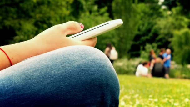 Close up of woman using mobile phone sitting in a park, hands only - Séquence, vidéo