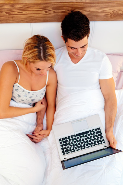 Couple with laptop in bed reading news - 写真・画像