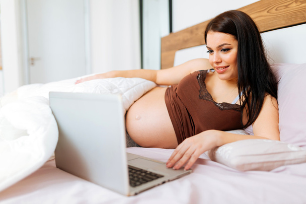Pregnant woman using laptop in bed - Фото, изображение