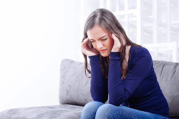 Młody kobieta siedzi na kanapie o migrenowy ból głowy - Zdjęcie, obraz