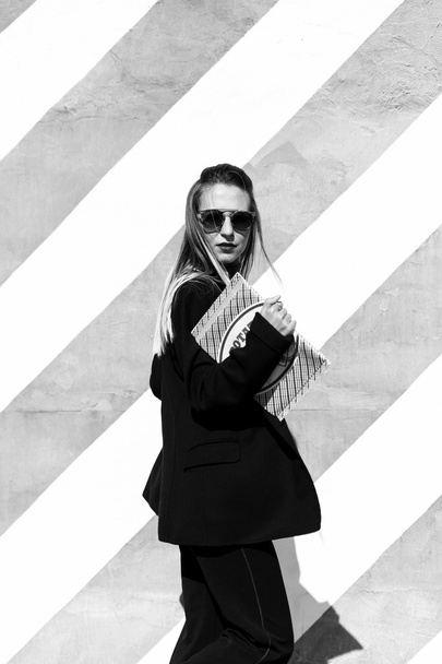 Beautiful fashionable young woman is standing near the striped wall and  holding a folder - Fotoğraf, Görsel