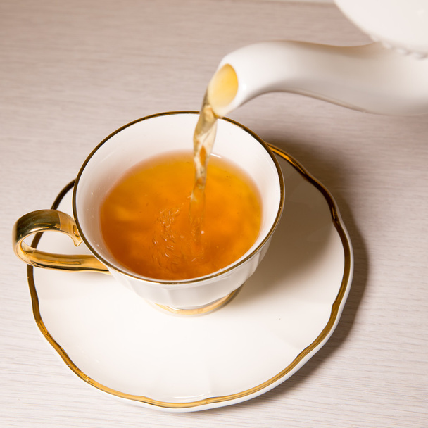 Чай наливають у чашку чаю, ізольований на білому тлі
. - Фото, зображення