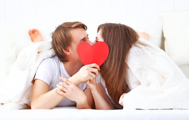 恋人のカップルがベッドで赤いハートとキス - 写真・画像