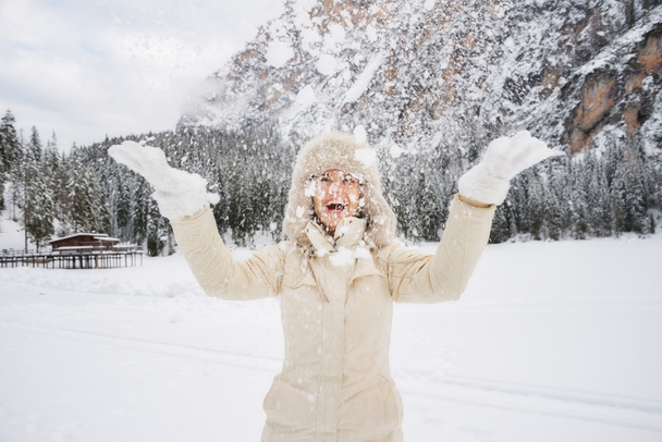 Happy woman in fur hat throwing up snow while standing outdoos - Fotografie, Obrázek