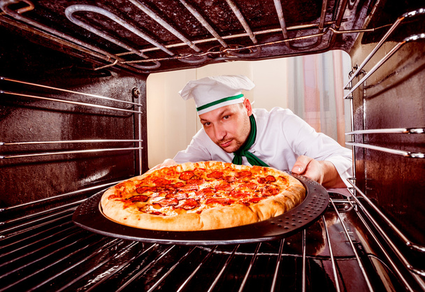 Chef prepares pepperoni pizza in the oven - Foto, Bild
