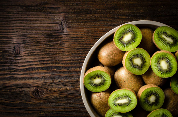 Kiwi fruits in bowl over wooden background - Zdjęcie, obraz