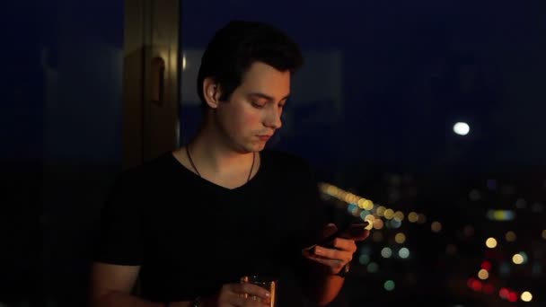Portré egy depressziós fiatalember segítségével a smartphone állva az ablak mellett - Felvétel, videó