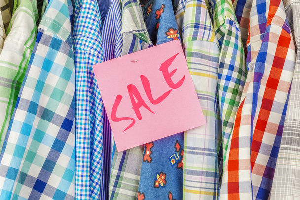 Row of hanging shirts with inscription SALE on paper sticker - 写真・画像