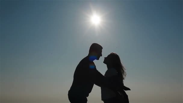 Középső lövés sziluettje boldog fiatal pár csók ölelgetés és kezében a háttérben az ég és a tenger - Felvétel, videó