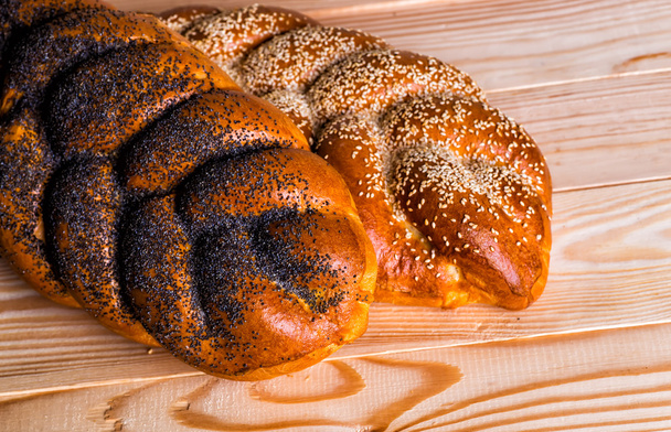 Two whole fresh challah bread with poppy and sesame on a wooden  - Foto, Imagen