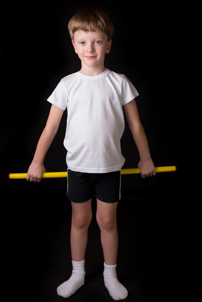 Boy athlete performs exercises with gymnastic stick in the gym - Fotó, kép