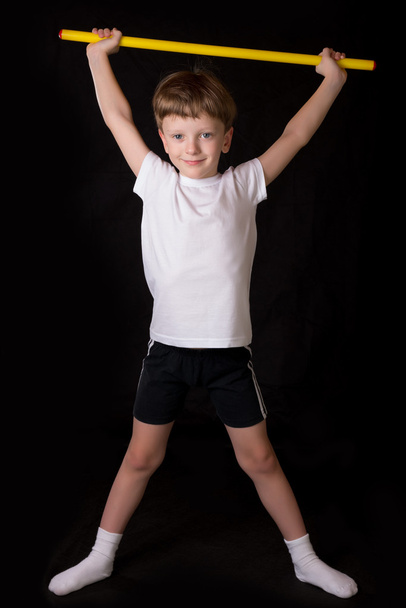 Мальчик-спортсмен выполняет упражнения с гимнастической палкой в тренажерном зале
 - Фото, изображение
