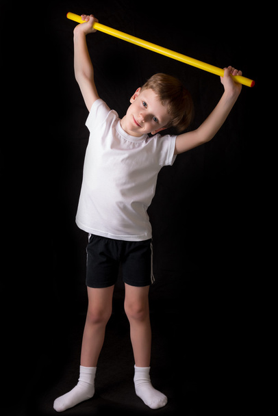 Boy athlete performs exercises with gymnastic stick in the gym - Foto, imagen