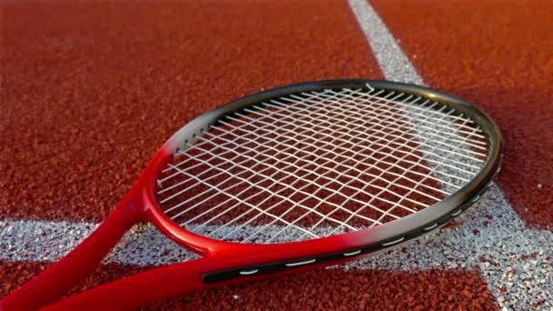 Ρακέτα του τένις που βρίσκεται στο κόκκινο γήπεδο τέννις, χέρι βάζει τρεις μπάλες του τένις σε αυτό - Πλάνα, βίντεο