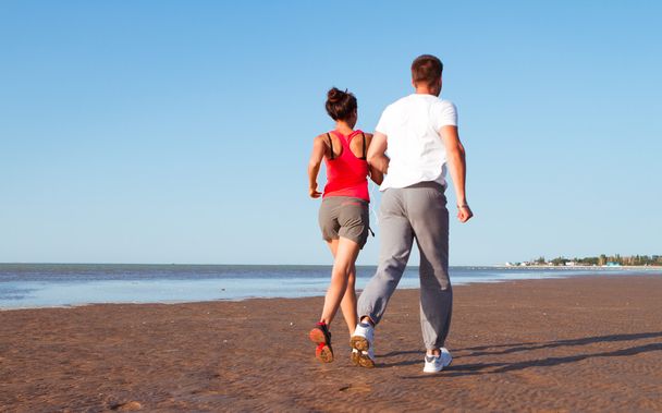 Young couple running together beside the water at the beach. Man - Photo, image