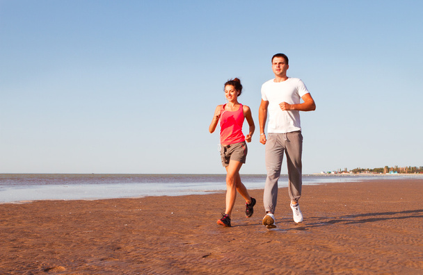 Young couple running together beside the water at the beach. Man - Photo, Image