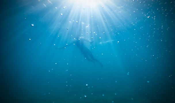Silhouette of female freediver floating through sunbeams. - Фото, зображення