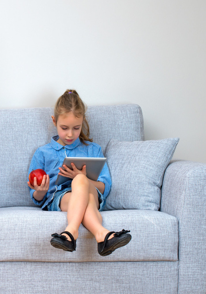 Little girl sitting on sofa and using tablet pc. Space for your text. - Photo, Image