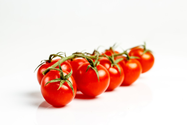 Гілка червоних помідорів лежить на білому столі
. - Фото, зображення
