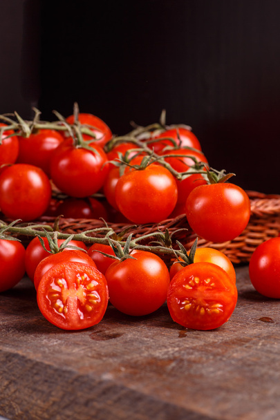 Gałąź czerwonych pomidorów leżącego w koszu na stół ciemny. - Zdjęcie, obraz