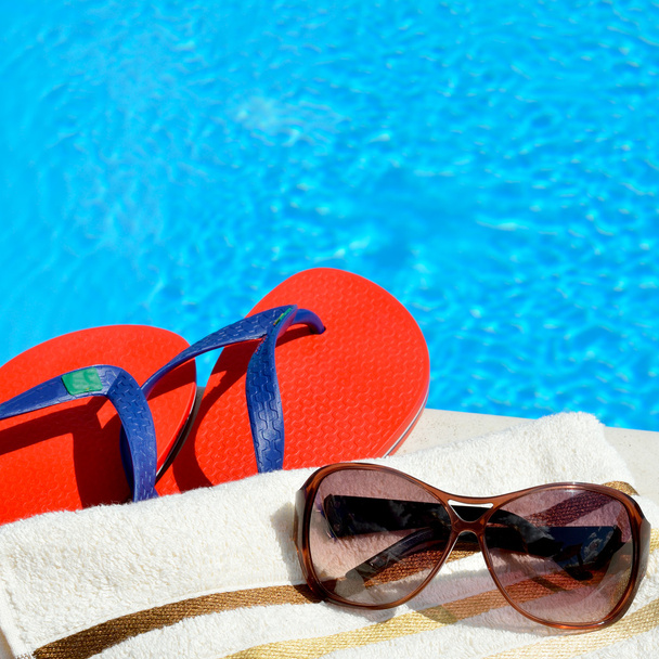 Сонцезахисні окуляри, пляжний рушник і фліп-флоп біля басейну
. - Фото, зображення
