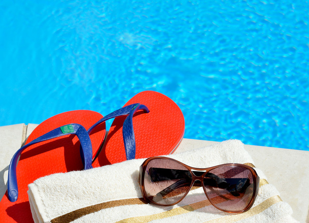 Sunglasses, beach towel and flip-flops by the swimming pool. - Foto, Bild