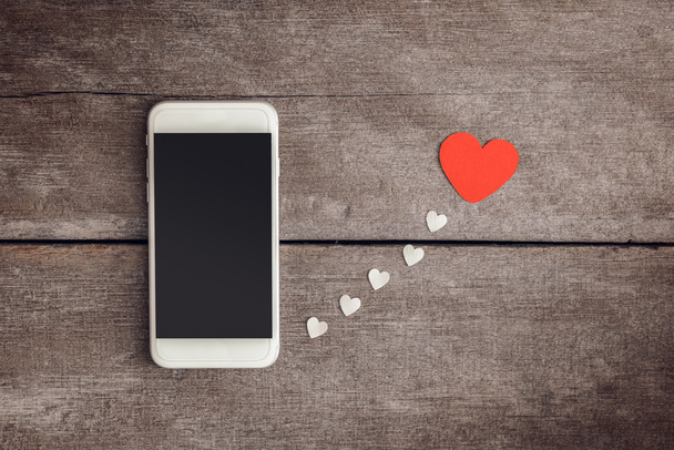 Smartphone and hearts paper on wooden background - Foto, Imagen