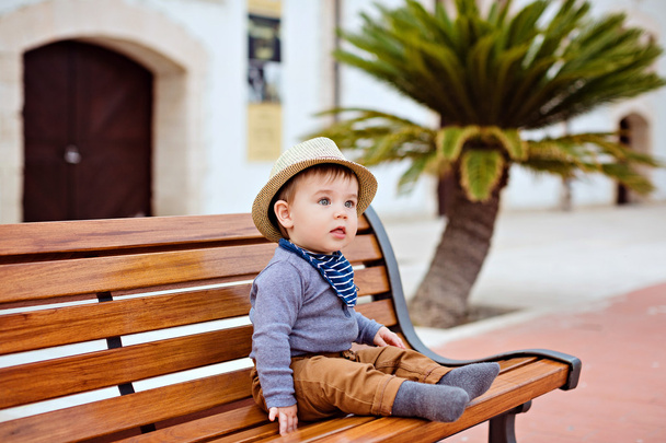 Little adorable baby boy in a straw hat and brown pants sitting  - Fotó, kép