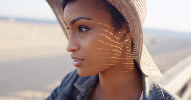 Zár megjelöl szemcsésedik-ból csinos fekete nő a tengerparton, széles karimájú kalap viselése - Fotó, kép