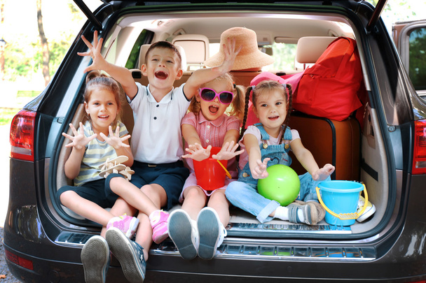 Three beautiful girls and boy sit on a car trunk and laughing - Foto, imagen