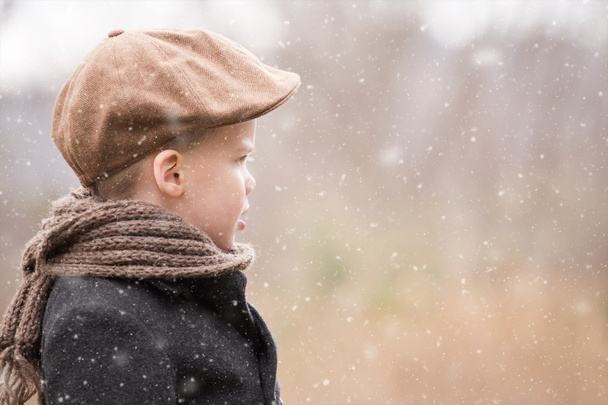 pikkulapsi poika pukeutunut lämpimästi katsellen eteenpäin ja miettien, kun sataa lunta
 - Valokuva, kuva