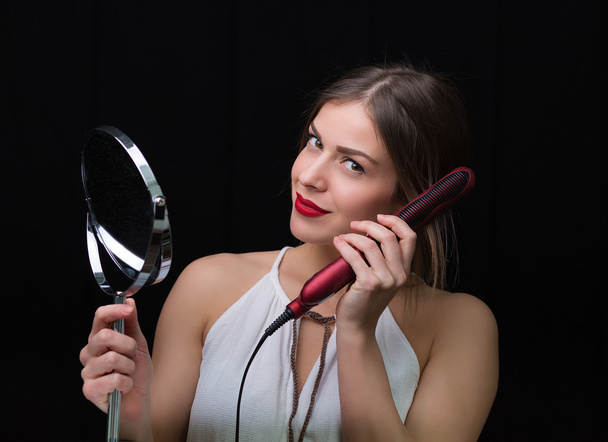 Vrouw met een spiegel en platte haren ijzer - Foto, afbeelding