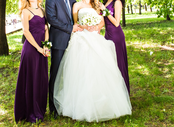 Bruid met de bruidegom en bruidsmeisjes in de buurt van bomen - Foto, afbeelding