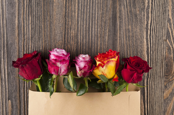 Bunch of multicolor rose flowers in paper envelope over wooden b - Φωτογραφία, εικόνα