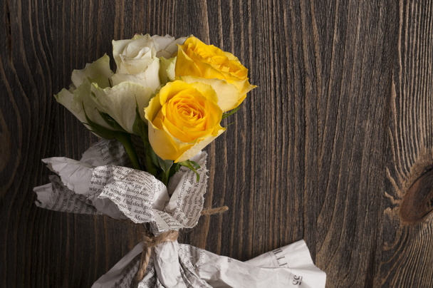 Bunch of multicolor rose flowers wrapped in newspaper over woode - 写真・画像