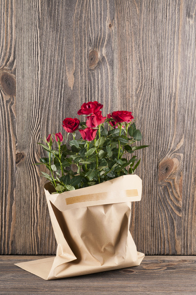 Red rose flowers in paper-bag on a wooden background - Fotografie, Obrázek